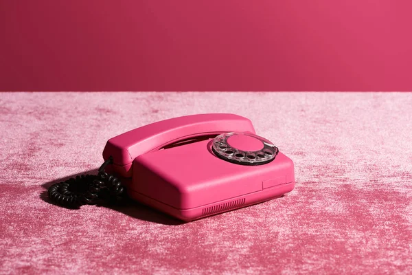 Teléfono vintage en tela de terciopelo rosa aislado en rosa, concepto femenino - foto de stock