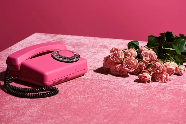 Ramo de rosas cerca del teléfono vintage en tela de terciopelo rosa aislado en rosa, concepto femenino - foto de stock