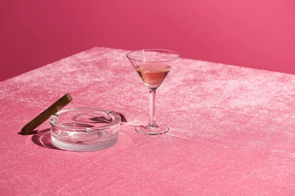 Roséwein im Glas neben Zigarre auf Aschenbecher auf samtrosa Tuch isoliert auf rosa, mädchenhaftes Konzept — Stockfoto