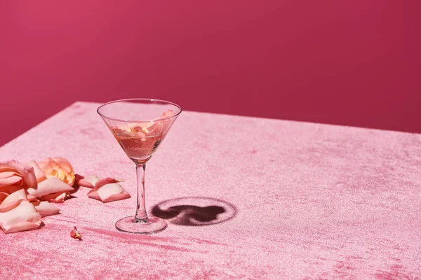 Rose petals near glass on velour pink cloth isolated on pink, girlish concept — Stock Photo