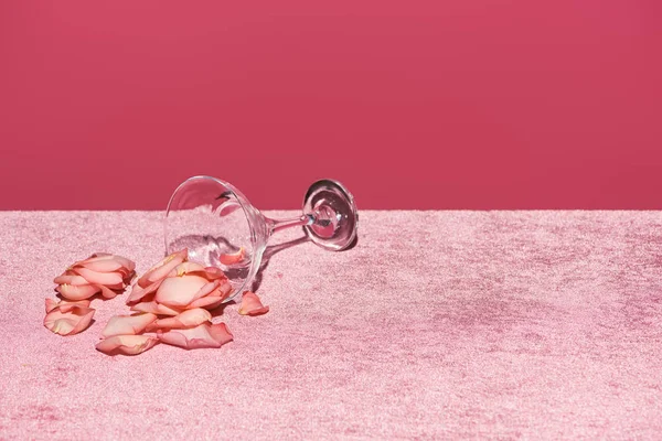 Pétalas de rosa perto de vidro em veludo pano rosa isolado em rosa, conceito feminino — Fotografia de Stock