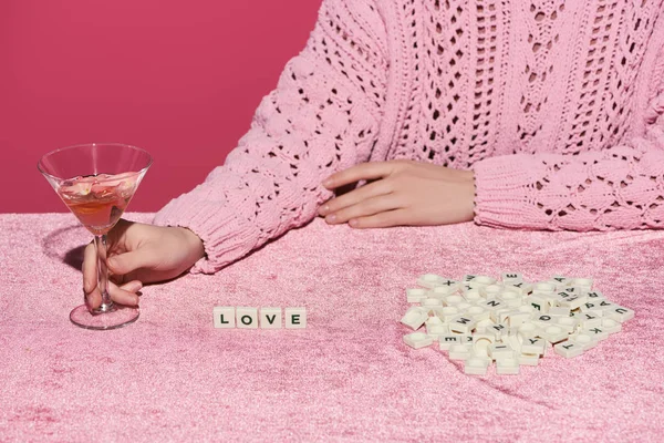 Vista cortada de mulher segurando vidro de vinho rosa em pano de veludo com letras de amor em cubos isolados em rosa, conceito feminino — Fotografia de Stock