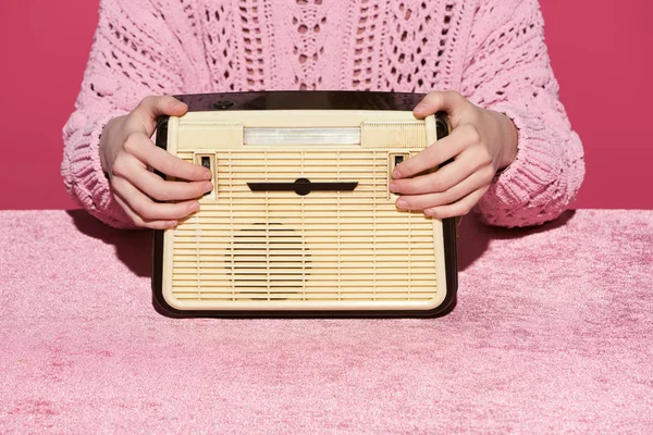 Обрезанный вид женщины, держащей винтажное радио на велюровой ткани, изолированной на розовой, девичьей концепции — стоковое фото