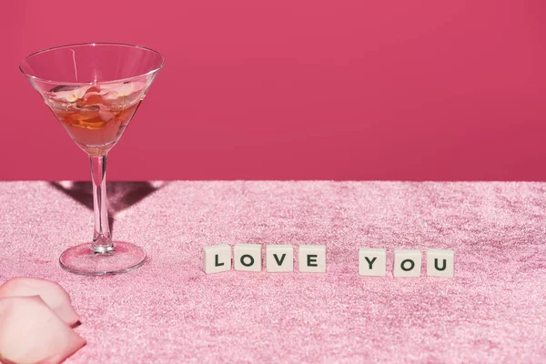 Rose petals in glass near cubes with love you lettering on velour pink cloth isolated on pink, girlish concept — Stock Photo