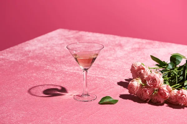 Vino rosato in vetro vicino bouquet di rose su velluto panno rosa isolato su rosa, concetto girlish — Foto stock