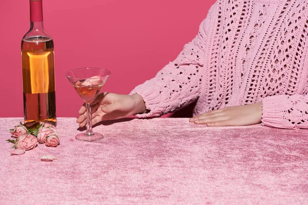 Vista recortada de la mujer sosteniendo vaso de vino de rosas cerca de rosas en tela de terciopelo aislado en rosa, concepto femenino - foto de stock