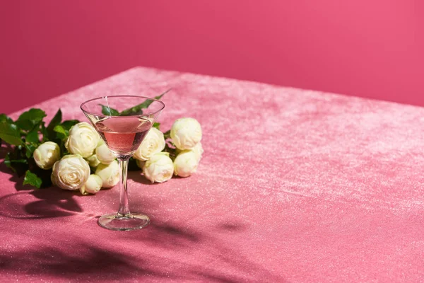 Vino rosato in vetro vicino bouquet di rose su velluto panno rosa isolato su rosa, concetto girlish — Foto stock