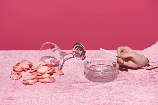 Cropped view of woman with cigarette and ashtray near glass with rose petals on velour cloth isolated on pink, girlish concept — Stock Photo