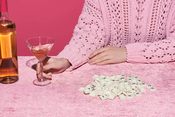 Vista recortada de la mujer sosteniendo vaso de vino rosa cerca de cubos con letras en tela de terciopelo aislado en rosa, concepto femenino - foto de stock