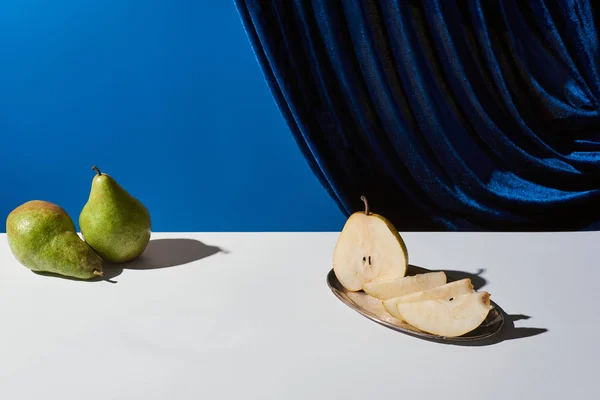 Classic still life with pear on silver plate on white table near velour curtain isolated on blue — Stock Photo