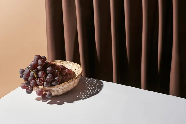 Классический натюрморт с виноградом в плетеной корзине на столе рядом с занавесом изолированы на бежевый — стоковое фото
