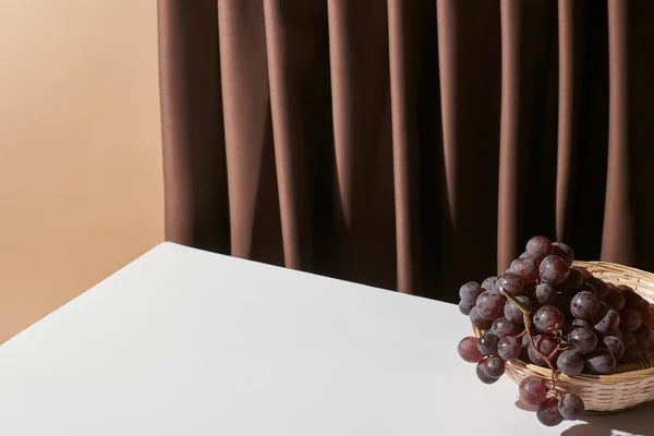 Classica natura morta con uva in vimini cesto sul tavolo vicino alla tenda isolato su beige — Foto stock