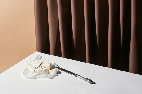 Classic still life with brie cheese and knife on table near curtain isolated on beige — Stock Photo