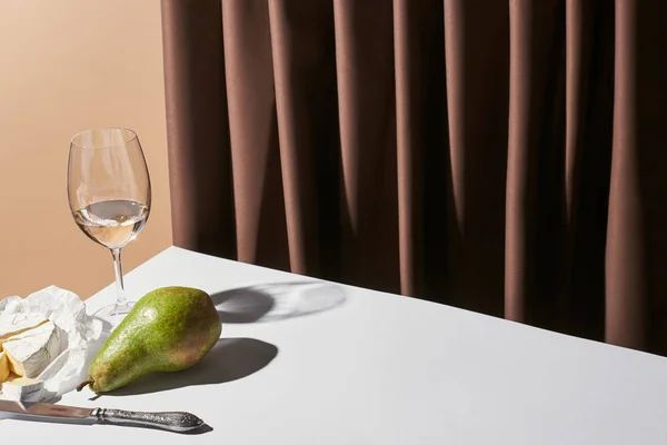 Vida tranquila clássico com queijo Camembert, vinho branco e pêra na mesa perto de cortina isolada em bege — Fotografia de Stock