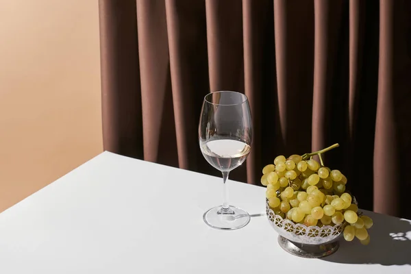 Vida tranquila clássico com uva e vinho branco na mesa perto de cortina isolada em bege — Fotografia de Stock