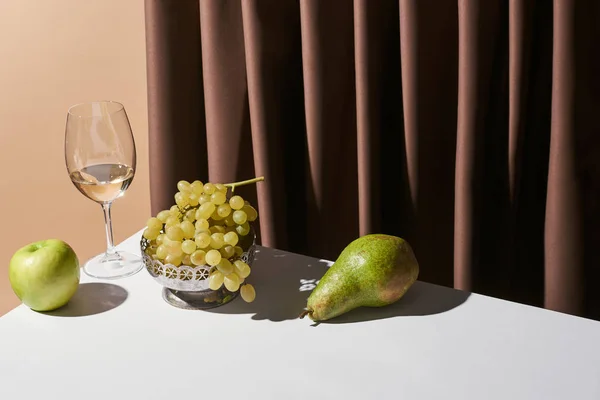 Классический натюрморт с белым вином и фруктами на столе рядом с занавесом изолированы на бежевый — стоковое фото