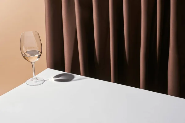 Classic still life with glass of white wine on table near curtain isolated on beige — Stock Photo