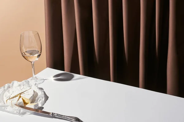 Bodegón clásico con queso Camembert y vino blanco en la mesa cerca de la cortina aislado en beige - foto de stock