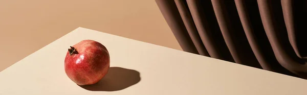 Classic still life with pomegranate on table near curtain isolated on beige, panoramic shot — Stock Photo