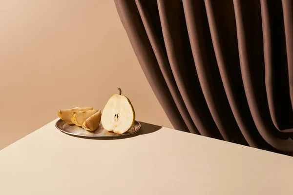 Classic still life with pear on silver plate on table near curtain isolated on beige — Stock Photo