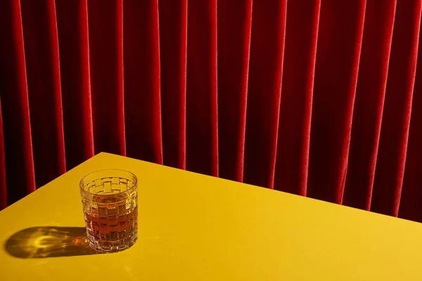 Classic still life with glass of drink on yellow table near red curtain — Stock Photo