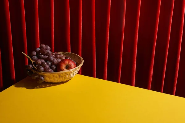 Vida tranquila clássico com frutas em cesta de vime na mesa amarela perto de cortina vermelha — Fotografia de Stock