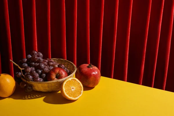 Классический натюрморт с фруктами в плетеной корзине на желтом столе рядом с красным занавесом — стоковое фото