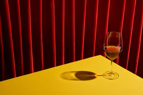 Classic still life with glass of red wine on yellow table near red curtain — Stock Photo
