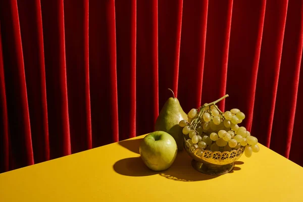 Clássico ainda vida com frutas verdes na mesa amarela perto de cortina vermelha — Fotografia de Stock