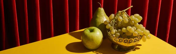 Classic still life with green fruits on yellow table near red curtain, panoramic shot — Stock Photo