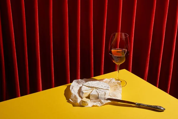 Classic still life with Camembert near glass of red wine on yellow table near red curtain — Stock Photo