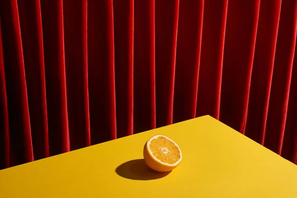 Natura morta classica con metà arancione su tavolo giallo vicino alla tenda rossa — Foto stock