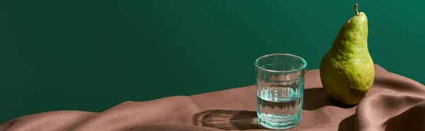 Vida tranquila clássico com pêra e água em vidro na mesa com toalha de mesa marrom isolado em verde, tiro panorâmico — Fotografia de Stock