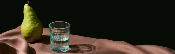 Classic still life with pear and water in glass on table with brown tablecloth isolated on black, panoramic shot — Stock Photo