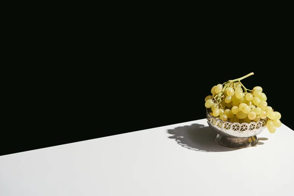 Bodegón clásico con uva en plato de plata con sombra sobre mesa blanca aislada sobre negro - foto de stock