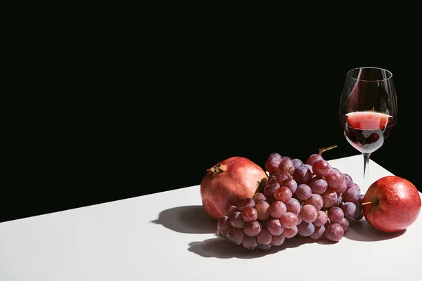 Nature morte classique avec des fruits et du vin rouge sur table blanche isolée sur noir — Photo de stock