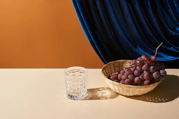 Classic still life with grape, glass on beige table near velour curtain isolated on orange — Stock Photo