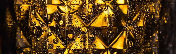 Vista de perto de vidro facetado geométrico com iluminação amarela em escuro, tiro panorâmico — Fotografia de Stock