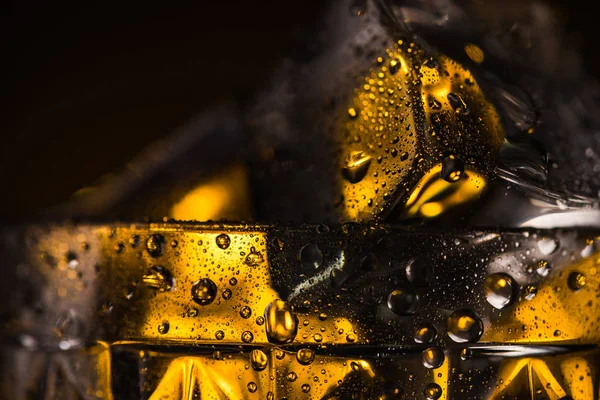 Vue rapprochée du glaçon carré en verre à facettes mouillé avec éclairage jaune — Photo de stock