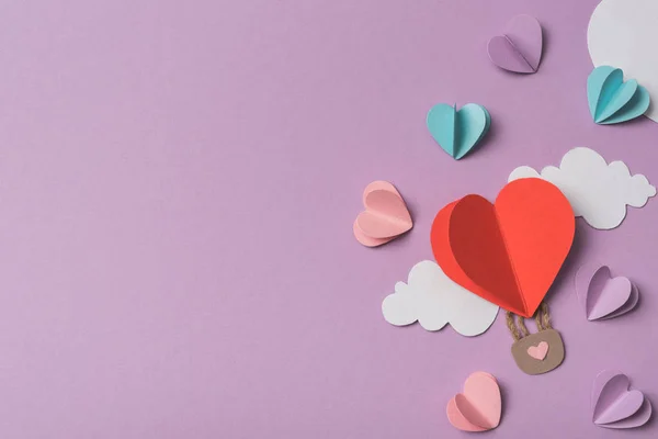 Vista dall'alto di cuori di carta colorati e nuvole intorno a palloncino d'aria di carta a forma di cuore su sfondo viola — Foto stock