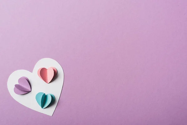 Vista superior de corazones de papel de colores en la tarjeta blanca sobre fondo violeta - foto de stock