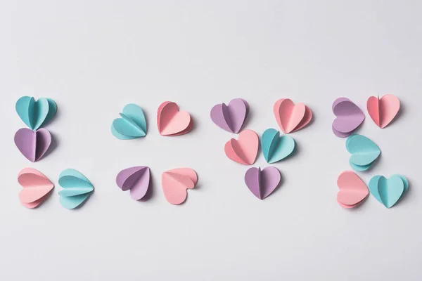 Vista superior de lettering amor feito de corações de papel coloridos no fundo branco — Fotografia de Stock