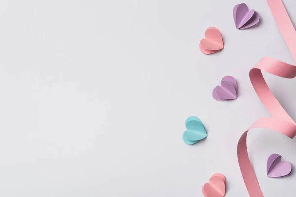 Vista superior de pequeños corazones de papel y remolino de papel rosa sobre fondo blanco - foto de stock