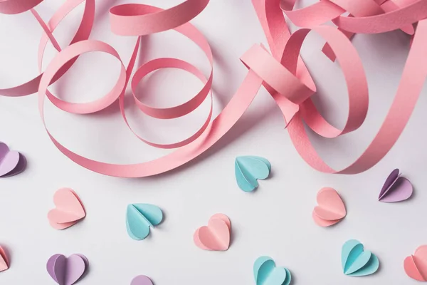 Draufsicht auf kleine Papierherzen und rosa Papierwirbel auf weißem Hintergrund — Stockfoto