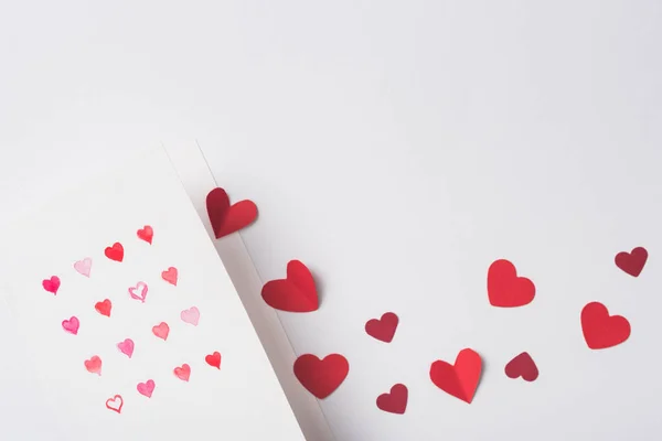 Vista dall'alto di biglietti di auguri di San Valentino e cuori rossi di carta su sfondo bianco — Foto stock