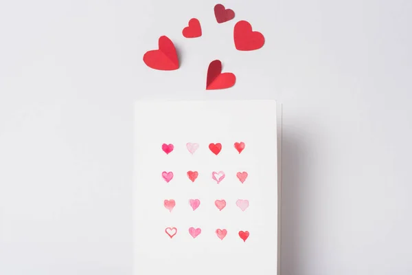 Vista superior de la tarjeta de felicitación de San Valentín y corazones rojos de papel sobre fondo blanco - foto de stock