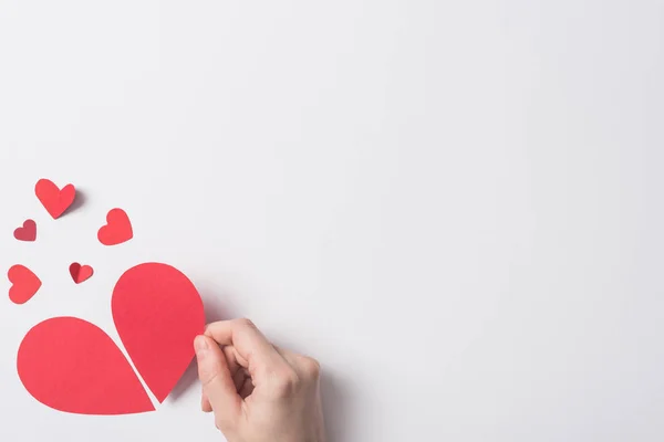 Cropped view of woman holding red broken heart pieces on white background — Stock Photo