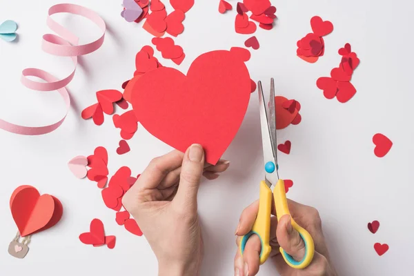 Vista recortada de la mujer sosteniendo el corazón rojo y tijeras sobre fondo blanco - foto de stock