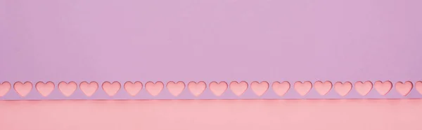 Top view of violet paper with cut out hearts on pink background, panoramic shot — Stock Photo