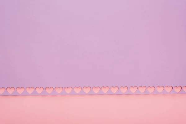 Vista superior de papel violeta con corazones cortados sobre fondo rosa - foto de stock